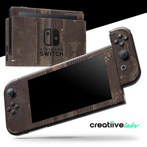 Puede incluir: Una consola Nintendo Switch y mandos con un diseño marrón estilo libro antiguo. La consola presenta el logotipo de Nintendo Switch y el texto "Nintendo Switch". El diseño incluye detalles florales dorados.