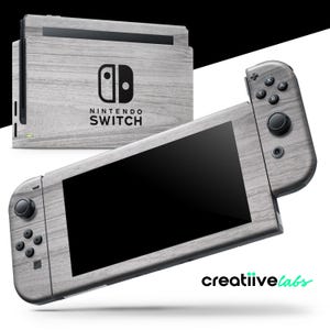 May include: A Nintendo Switch console and controllers with a light gray wood grain design. The console has the Nintendo Switch logo and the text "NINTENDO SWITCH". The controllers have black buttons and joysticks. The brand name "creatiive labs" is in the bottom right corner.
