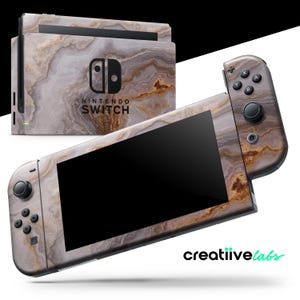 May include: A Nintendo Switch console and controllers with a marble-like design. The console and controllers have a pattern of gray, brown, and white swirls. The Nintendo Switch logo is visible on the console.