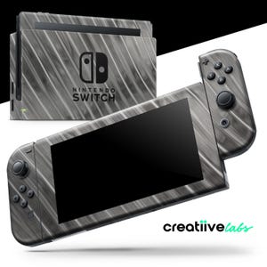 Puede incluir: Una consola y mandos Nintendo Switch con un diseño de vetas de madera grises. La consola y los mandos se muestran sobre un fondo blanco. El logotipo de Nintendo Switch es visible.