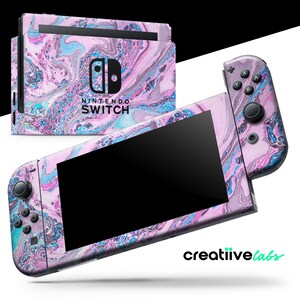 May include: A Nintendo Switch console and controllers with a custom skin featuring a swirling pattern of pink, blue, and white. The console and controllers are displayed against a white background. The text "NINTENDO SWITCH" is visible on the console.