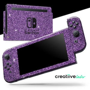 Pode incluir: Uma consola Nintendo Switch e comandos cobertos de glitter roxo. A consola e os comandos têm um acabamento brilhante e texturizado. O logótipo da Nintendo Switch é visível na consola. A imagem está sobre um fundo branco e preto.