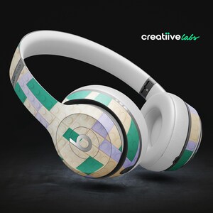 May include: White wireless headphones with a green, purple, and white patterned design. The headphones have a large, round earcup and a smaller, round earcup.
