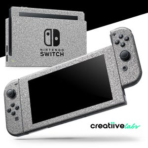 May include: A Nintendo Switch console and controllers with a textured, glittery silver finish. The console features the Nintendo Switch logo and the text "NINTENDO SWITCH". The controllers have black buttons and joysticks.