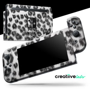 Pode incluir: Consola e comandos Nintendo Switch com um design de padrão de leopardo a preto e branco. A consola e os comandos são exibidos num fundo branco. O logótipo Nintendo Switch é visível.