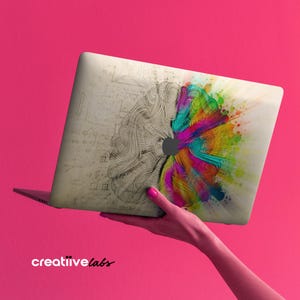 May include: A laptop computer with a colorful brain design on the cover. The design features a half-brain with a detailed, sketched style and a half-brain with a colorful, abstract style. The laptop is open and the screen is black.