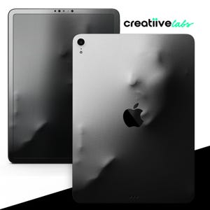 May include: Black and white iPad skin with a textured, abstract design that resembles a face. The Apple logo is visible in the center of the skin.