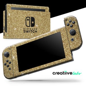 以下が含まれることがあります： 金色のグリッターNintendo Switchコンソールとコントローラー。コンソールとコントローラーは金色のグリッターで覆われており、コンソールにはNintendo Switchのロゴがあります。コントローラーには黒いボタンとジョイスティックがあります。「Nintendo Switch」の文字がコンソールに印刷されています。