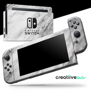 以下が含まれることがあります： 白とグレーの大理石模様のNintendo Switch本体とコントローラー。本体にはNintendo Switchのロゴと文字が入っています。コントローラーには黒いボタンとジョイスティックが付いています。画像には「creatiivelabs」の文字も含まれています。