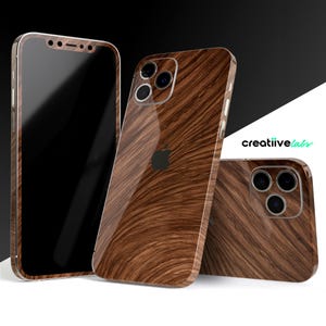 Op de afbeelding: Drie iPhone-hoesjes met een houtnerfdesign. De hoesjes zijn bruin en hebben een glanzende afwerking. Het hoesje links is zwart en heeft een transparante schermbeschermer. Het hoesje rechts heeft een camera-uitsparing. De tekst "creativelabs" is zichtbaar op de achtergrond.