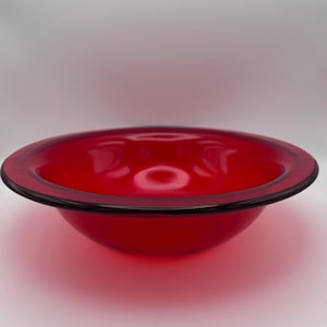 May include: A vibrant red glass bowl with a dark rim. The bowl has a rounded shape and a smooth, glossy surface. The bowl is likely used for serving or display.