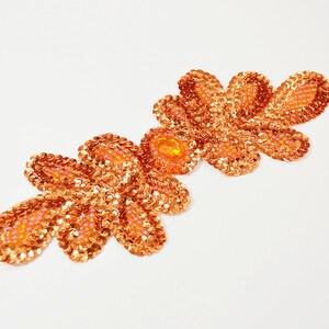 Peut inclure: Une applique en sequins de couleur cuivre en forme de trois fleurs stylisées. L'applique est faite de petits sequins irisés cousus ensemble pour créer un effet chatoyant.