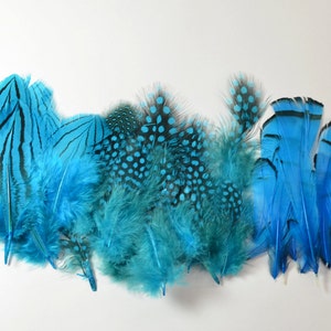 Puede incluir: Una colección de plumas azules con diferentes patrones, incluyendo lunares, rayas y colores sólidos. Las plumas están dispuestas en una fila sobre un fondo blanco.