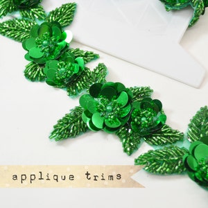 Peut inclure: Garniture de perles vertes avec des fleurs en sequins. La garniture est faite de petites perles et de sequins verts, et présente un motif répétitif de fleurs avec des feuilles. La garniture est parfaite pour ajouter une touche d'élégance à tout projet.