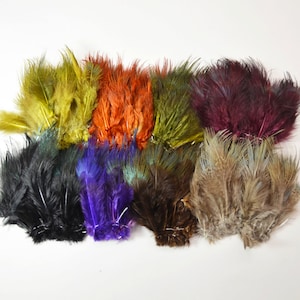 May include: Assortment of ten bundles of dyed pheasant tail feathers in various colours, including black, brown, green, purple, red, and yellow.