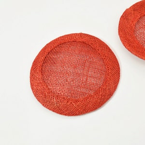 May include: Two round, woven, orange-red hat bases. The bases have a circular shape with a woven mesh center and a thicker, rounded edge. The items are set against a white background.