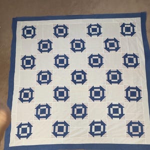 May include: A square quilt featuring a repeating pattern of dark blue geometric shapes on a white background. The design consists of central squares surrounded by four arrow-like motifs, all framed by a solid dark blue border.