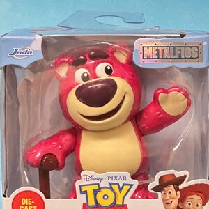 May include: A die-cast Lotso figure from Disney Pixar's Toy Story, packaged in a clear plastic box. The figure is a pink bear with a brown nose and a tan belly. The box features the Metalfigs logo and the Toy Story logo.