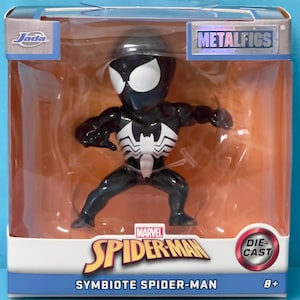 May include: A Jada Metalfigs die-cast Symbiote Spider-Man figure in a clear window box. The figure is black with a large white spider emblem on the chest and white eyes. The packaging features the Marvel Spider-Man logo and an 8+ age rating.