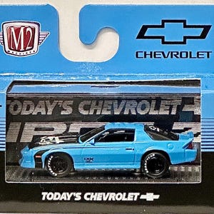 May include: A blue die-cast model car of a Chevrolet Camaro, packaged in a box with the Chevrolet logo and "TODAY'S CHEVROLET" text. The model car is light blue with black accents and Goodyear tires.