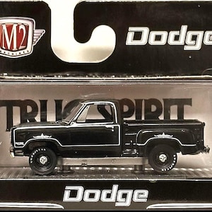 May include: A black Dodge pickup truck model in a display box. The truck has white accents and the text "TRUE SPIRIT" is visible. The box features the "M2 Machines" logo and the word "Dodge".