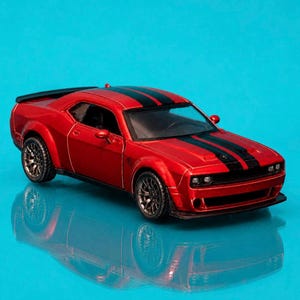 May include: A red toy car with black racing stripes on the hood and roof. The car has black wheels and a spoiler. The car is a miniature replica of a sports car.