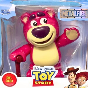 May include: A die-cast Lotso figure from the Disney Pixar Toy Story franchise. The pink bear has a yellow belly and a purple nose. The figure is in a clear plastic package with the Metalfigs logo and the Toy Story logo.