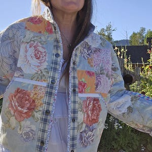Peut inclure: Veste matelassée avec un motif patchwork à motifs floraux dans les tons de rose, pêche et bleu. La veste a une fermeture boutonnée sur le devant, des poches et des accents à carreaux. Les manches ont un poignet à motifs.