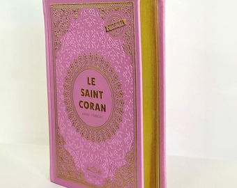May include: A pink and gold hardcover book with the title "LE SAINT CORAN" in gold lettering. The book is embossed with intricate floral patterns and has a gold spine.