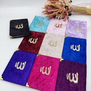 May include: A selection of velvet-covered books in various colours, including black, blue, pink, purple, and burgundy. Each book has gold corner accents and gold Arabic calligraphy. A bouquet of dried flowers is visible in the background.