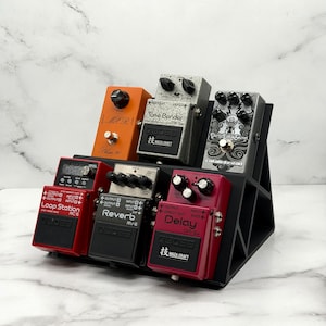 Puede incluir: Una colección de pedales de efectos para guitarra en varios colores, incluyendo rojo, naranja y gris. Los pedales están colocados en un soporte negro. Los pedales tienen perillas y conectores de entrada/salida.