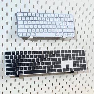 May include: Two wireless keyboards, one white with a black keycap and one black with a white keycap, are mounted on a white pegboard wall.