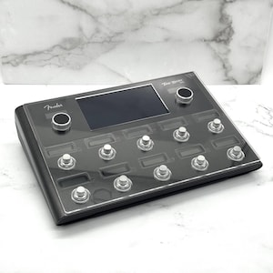 May include: A dark gray Fender Tone Master Pro guitar effects processor. It features a central screen, two knobs, and numerous silver footswitches. The Fender logo is visible on the top left.