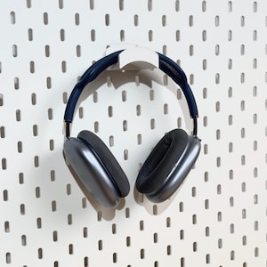 May include: A pair of gray over-ear headphones with a white hook hanging on a white pegboard wall.