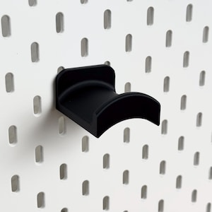 May include: Black plastic pegboard hook with a curved design. The hook is mounted on a white pegboard.