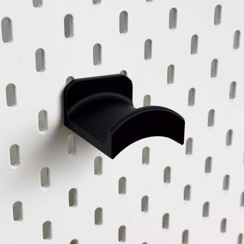 May include: Black plastic pegboard hook with a curved design. The hook is mounted on a white pegboard.