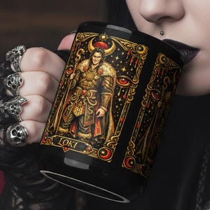 May include: Black ceramic mug with a detailed illustration of Loki in gold, red, and brown tones. The design includes the word "LOKI" at the bottom. The mug has a dark background and is held by a person.