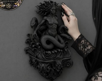 May include: A black sculpture of a woman with snakes, mounted on a wall. The sculpture has intricate details and is surrounded by decorative elements. The image includes the text "DIGITAL FILE FOR 3D PRINTING".