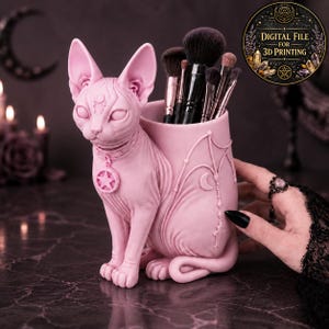 Può includere: Un organizer da scrivania rosa chiaro a forma di gatto Sphynx con un supporto cilindrico sul dorso. Il gatto indossa un collare con un ciondolo a pentagramma e ha un simbolo di luna crescente sulla fronte. Il supporto è decorato con motivi in rilievo di ali e lune.