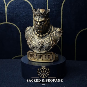 Pode incluir: Um busto dourado de um orco usando uma coroa e uma armadura ornamentada. O busto está em uma base preta com as palavras "SACRED & PROFANE" e "JWL" escritas nela.