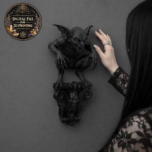 Puede incluir: Una escultura de gárgola negra con alas extendidas, posada sobre un pedestal decorativo. La escultura está montada en una pared gris. Una pegatina circular con el texto "DIGITAL FILE FOR 3D PRINTING" está en la esquina superior izquierda.