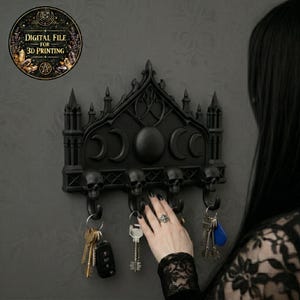 May include: Black gothic-style key holder with skull hooks and a decorative arched top featuring crescent moons and a central sphere. The key holder is mounted on a gray wall, with keys hanging from the hooks. The text "DIGITAL FILE FOR 3D PRINTING" is in a circular graphic.