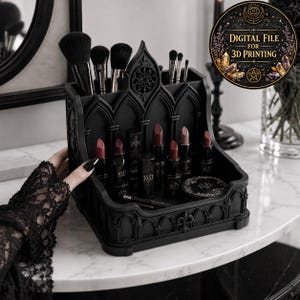 Peut inclure: Un organisateur de maquillage noir de style gothique avec plusieurs compartiments. Il contient divers pinceaux de maquillage et rouges à lèvres dans des tons rouges et bruns. Le design est orné et posé sur une surface en marbre.