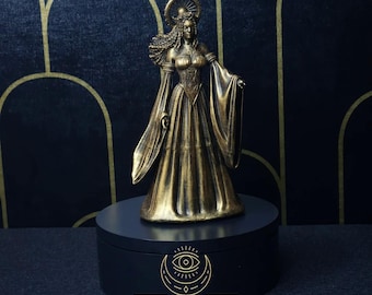 May include: Gold-toned statue of a woman wearing a crown and flowing gown. The statue is on a black circular base with the text "SACRED & PROFANE" and "JWL" printed on it.