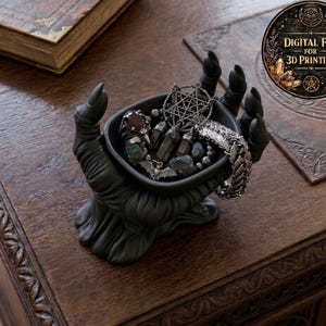 May include: A black hand-shaped jewelry dish filled with rings, crystals, and a bracelet. The dish is holding various accessories. The image also includes a book and a circular graphic with the text "DIGITAL FILE FOR 3D PRINTING".