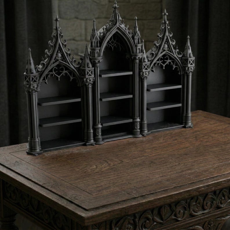 May include: A black, gothic-style bookshelf with three arched sections and multiple shelves. The bookshelf is made of a dark material and sits on a wooden table. The design features intricate architectural details.