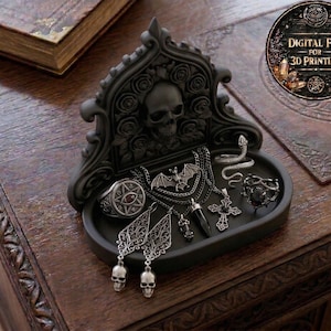 Peut inclure: Un présentoir à bijoux gothique noir avec un crâne et des roses, contenant divers colliers, bagues et boucles d'oreilles argentés. Le présentoir comprend un pendentif chauve-souris, une bague serpent et des boucles d'oreilles tête de mort. Un livre et un fichier numérique pour l'impression 3D sont également présents.