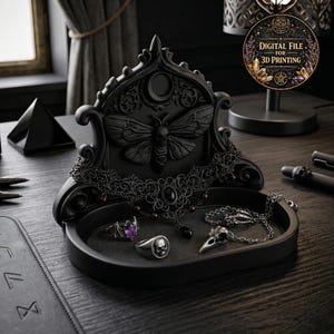 May include: A black jewelry tray with a moth design on the back. The tray holds a black necklace, rings, and a skull pendant necklace. The tray has a round shape and is made of a dark material. The image also includes a digital file for 3D printing.