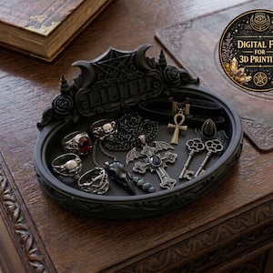 May include: A black decorative tray with the name "LILITH" on it, filled with gothic-themed jewelry. The tray holds rings, necklaces, a choker, and key-shaped earrings. A digital file for 3D printing is also visible.