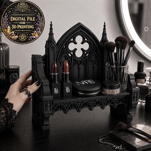 Puede incluir: Organizador de maquillaje negro de estilo gótico con un estante que contiene barras de labios, una polvera y brochas de maquillaje. El organizador tiene un diseño arqueado decorativo. Se muestra un archivo digital para impresión 3D.